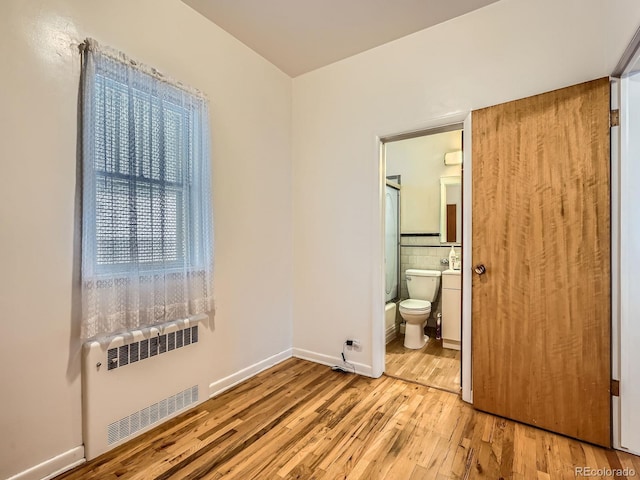 unfurnished bedroom with ensuite bathroom, radiator heating unit, and light wood-type flooring