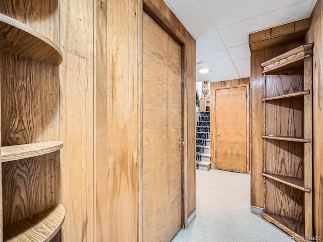 hallway featuring a paneled ceiling, light colored carpet, and wooden walls