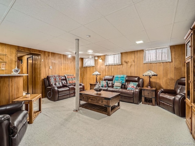 carpeted living room with wooden walls and a drop ceiling