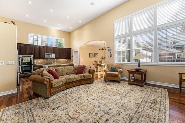 living room featuring baseboards, a high ceiling, arched walkways, and dark wood-type flooring