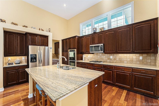 kitchen with a sink, light stone countertops, appliances with stainless steel finishes, and wood finished floors