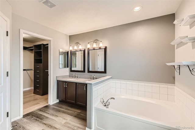 bathroom with a garden tub, visible vents, a spacious closet, vanity, and wood finished floors