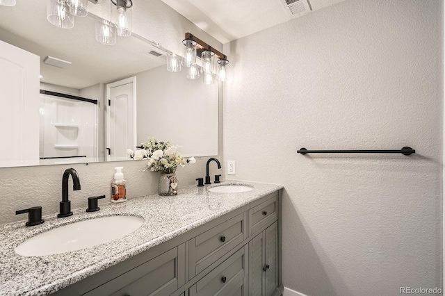 bathroom with a textured wall, visible vents, a sink, and double vanity