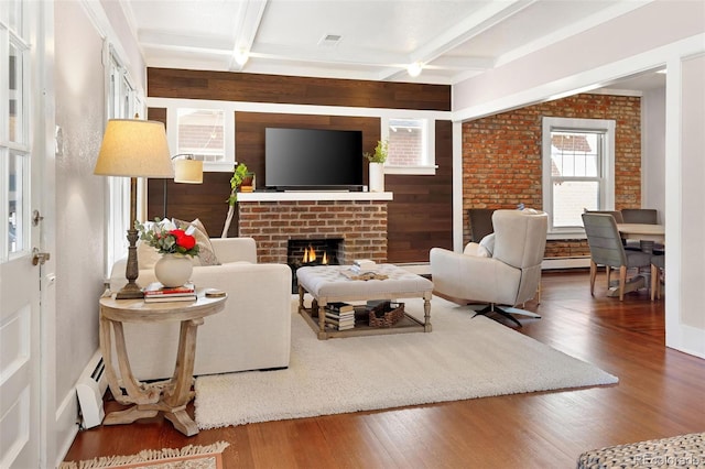 living area with beam ceiling, coffered ceiling, a fireplace, and wood finished floors