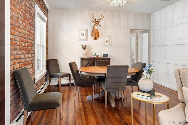 dining room featuring a healthy amount of sunlight, brick wall, wood-type flooring, and a baseboard heating unit