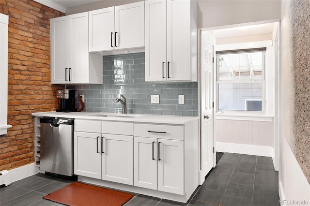 kitchen featuring light countertops, stainless steel dishwasher, white cabinetry, a sink, and dark tile patterned floors