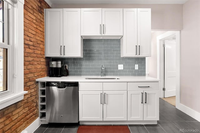 kitchen featuring light countertops, stainless steel dishwasher, dark tile patterned floors, and a sink