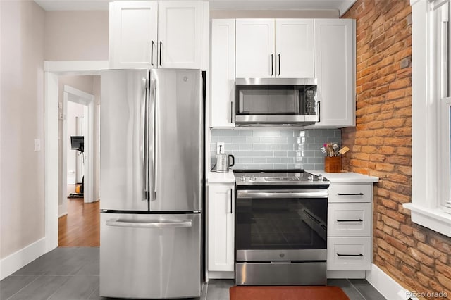 kitchen featuring brick wall, white cabinetry, light countertops, appliances with stainless steel finishes, and tasteful backsplash