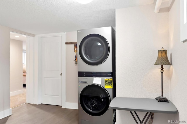 laundry area featuring a textured ceiling, wood finished floors, stacked washer and clothes dryer, and baseboards