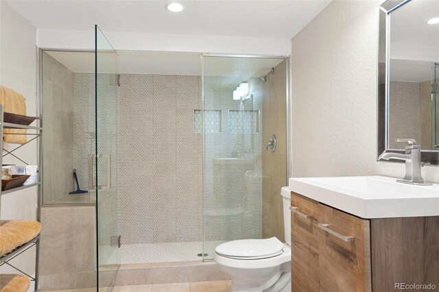 full bath with a textured wall, toilet, tile patterned flooring, vanity, and a shower stall