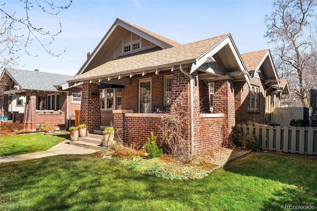 view of front of house with roof with shingles, a front yard, fence, and brick siding