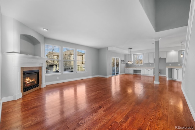 unfurnished living room with decorative columns, a tile fireplace, and light wood-type flooring