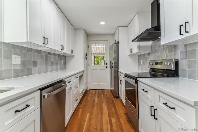 kitchen featuring stainless steel appliances, wood-type flooring, white cabinets, and wall chimney exhaust hood