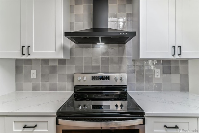 kitchen with wall chimney range hood, stainless steel electric range oven, white cabinets, and backsplash