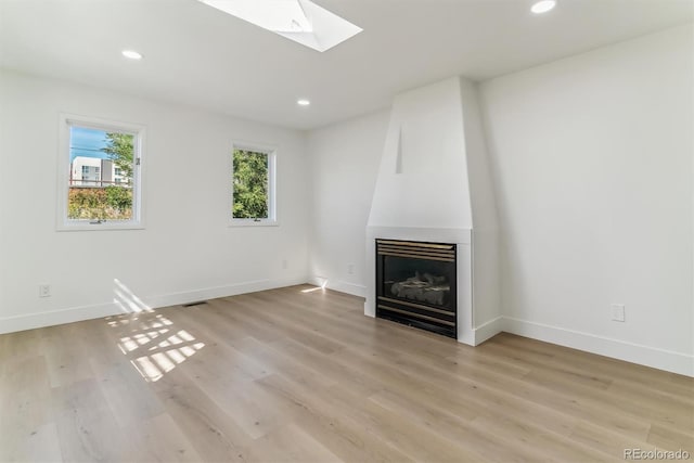 unfurnished living room featuring a skylight, light wood-type flooring, and a fireplace