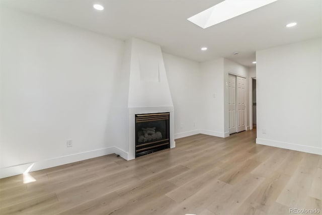 unfurnished living room with a skylight, light wood-type flooring, and a large fireplace