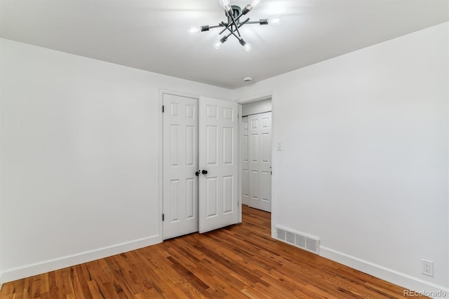 unfurnished bedroom featuring hardwood / wood-style flooring and a chandelier