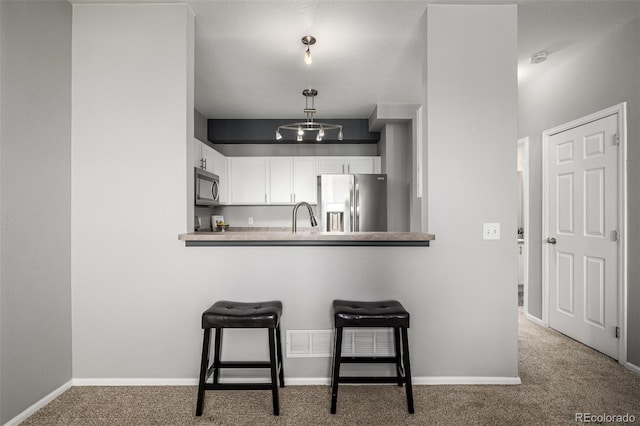 kitchen featuring white cabinets, a kitchen breakfast bar, light colored carpet, kitchen peninsula, and stainless steel appliances