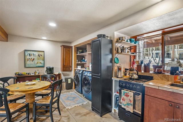 kitchen featuring tile countertops, washer and clothes dryer, open shelves, brown cabinetry, and gas stove