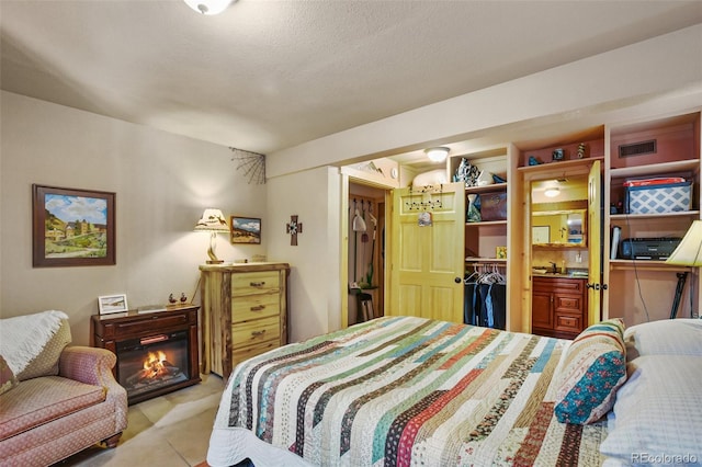 tiled bedroom featuring a spacious closet, a textured ceiling, and a glass covered fireplace