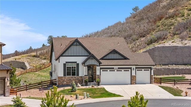 craftsman-style home featuring fence, stone siding, board and batten siding, an attached garage, and driveway