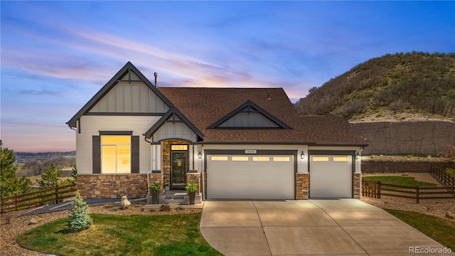 craftsman inspired home with driveway, roof with shingles, fence, an attached garage, and stone siding