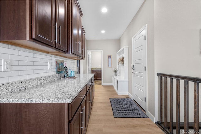 interior space featuring light wood-type flooring, decorative backsplash, dark brown cabinets, and light stone countertops