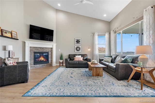 living room featuring a ceiling fan, a brick fireplace, wood finished floors, and high vaulted ceiling