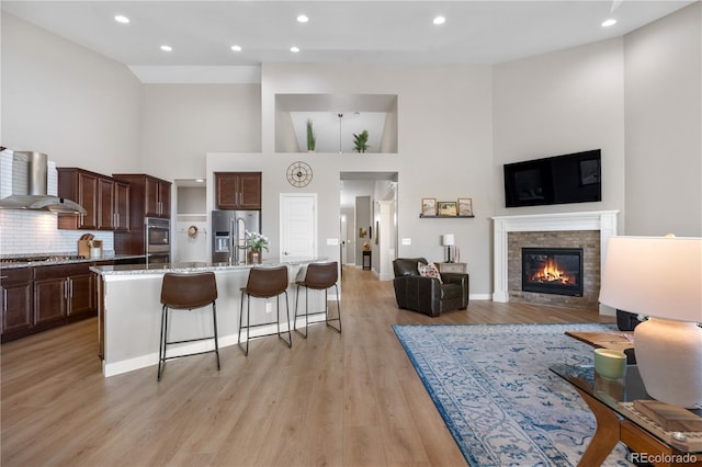 living area with recessed lighting, a glass covered fireplace, light wood finished floors, and a towering ceiling