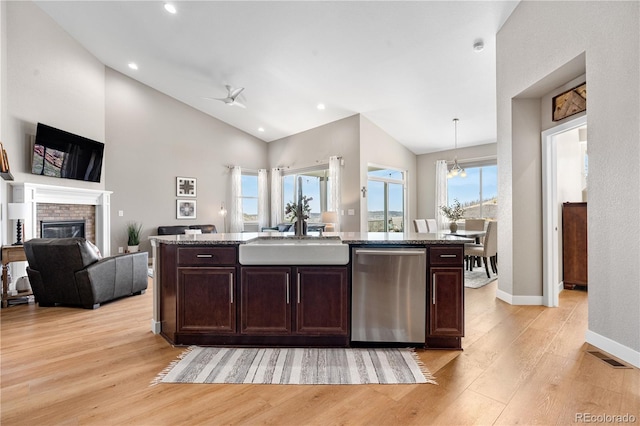 kitchen featuring a ceiling fan, stainless steel dishwasher, a sink, stone countertops, and light wood-style flooring