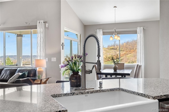 kitchen with a chandelier, hanging light fixtures, a sink, stone countertops, and lofted ceiling
