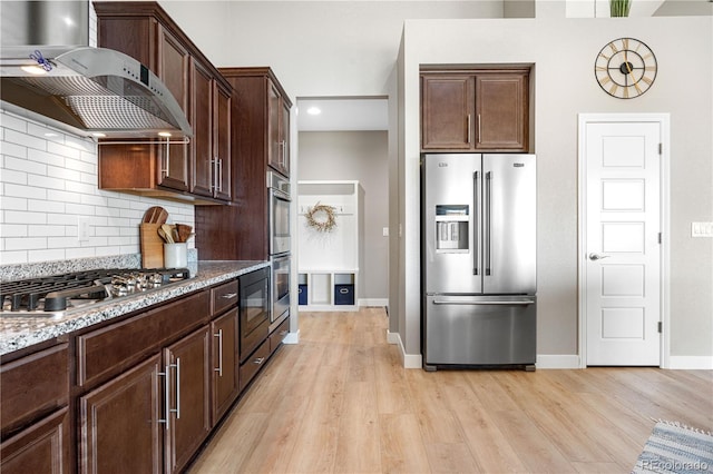 kitchen featuring light wood-type flooring, decorative backsplash, wall chimney exhaust hood, and stainless steel appliances