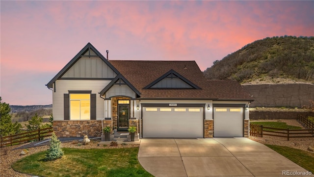 craftsman house with fence, an attached garage, stone siding, board and batten siding, and driveway