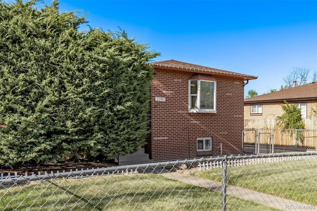 view of property exterior featuring fence, a lawn, and brick siding