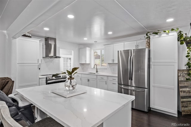 kitchen featuring wall chimney range hood, recessed lighting, white cabinets, a sink, and appliances with stainless steel finishes
