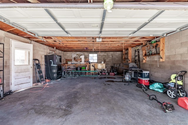 garage with freestanding refrigerator and concrete block wall