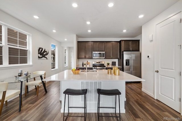 17848 Gallup St, Broomfield, CO 80023 - kitchen featuring stainless steel appliances, dark brown cabinetry, a breakfast bar area, a center island with sink, and dark wood finished floors