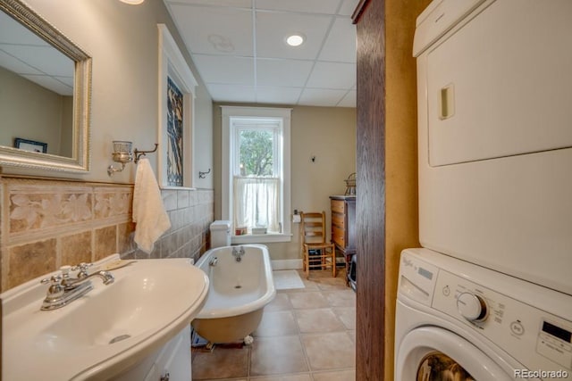 bathroom with a paneled ceiling, tile patterned floors, sink, stacked washer / drying machine, and a tub