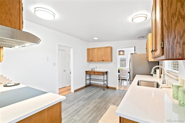 kitchen featuring stainless steel fridge, light wood-type flooring, cooktop, island range hood, and sink