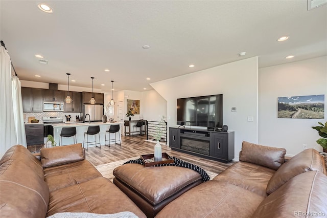 living area featuring visible vents, recessed lighting, light wood-style floors, and a glass covered fireplace