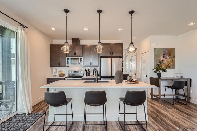 kitchen with dark brown cabinets, dark wood finished floors, a kitchen breakfast bar, stainless steel appliances, and a sink