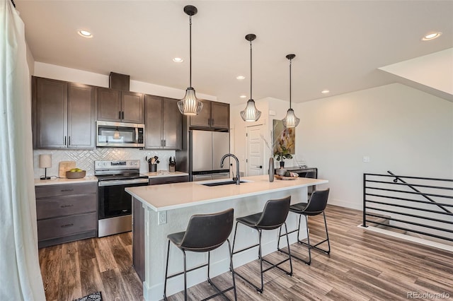 kitchen featuring dark wood-style floors, a breakfast bar, a sink, stainless steel appliances, and tasteful backsplash