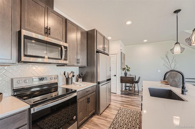 kitchen featuring tasteful backsplash, light countertops, light wood-style floors, stainless steel appliances, and a sink