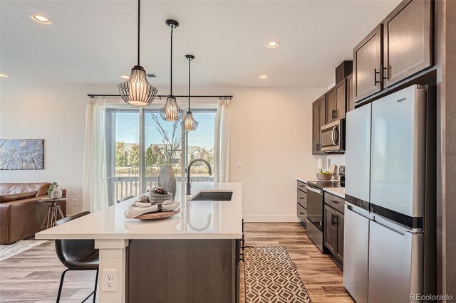 kitchen with dark brown cabinets, light wood-type flooring, light countertops, appliances with stainless steel finishes, and a sink