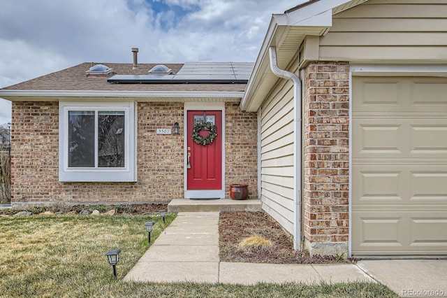 doorway to property featuring brick siding, solar panels, roof with shingles, and an attached garage