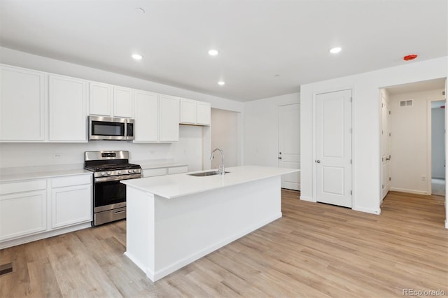 kitchen featuring sink, a center island with sink, stainless steel appliances, light hardwood / wood-style floors, and white cabinets