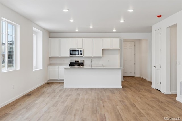 kitchen with white cabinetry, stainless steel appliances, a center island with sink, and light hardwood / wood-style flooring