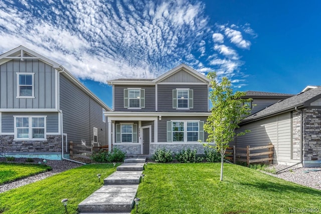 craftsman inspired home with board and batten siding, stone siding, fence, and a front lawn