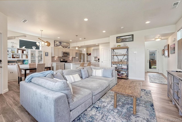 living area with light wood-style floors, visible vents, and a notable chandelier