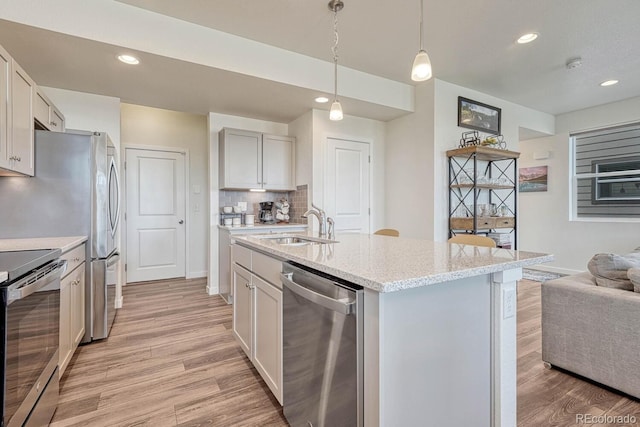 kitchen with stainless steel appliances, light wood-type flooring, hanging light fixtures, and a sink